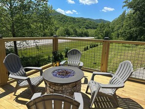 Una terraza con una mesa y sillas alrededor de una chimenea, con vistas a un área verde y montañas.