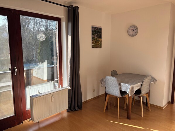 Un coin repas avec une table et des chaises, un radiateur, une fenêtre avec des rideaux et une horloge au mur.