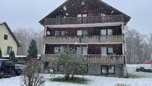 Un edificio de varios pisos con balcones, rodeado de nieve en el suelo y árboles.