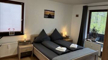 Ein Schlafzimmer mit Bett, Nachttischen, einer Lampe, einem Bild an der Wand und einem Fenster mit Vorhängen.