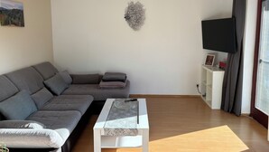 Una sala de estar moderna con un sofá seccional gris, una mesa de centro blanca y un televisor montado en la pared.