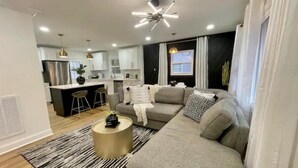 Ein modernes Wohnzimmer mit einem grauen Sofa, einem runden Couchtisch und einem schwarz-weißen Streifen Teppich.