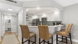 Een moderne keuken met witte kasten, een roestvrijstalen koelkast, een magnetron en een groot kookeiland met barstoelen.