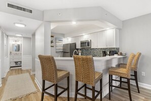 Una cocina moderna con armarios blancos, un refrigerador de acero inoxidable, un microondas y una isla grande con taburetes de bar.