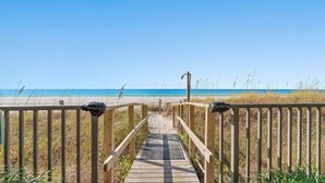 Een houten looppad dat naar een strand leidt, met een helderblauwe lucht.