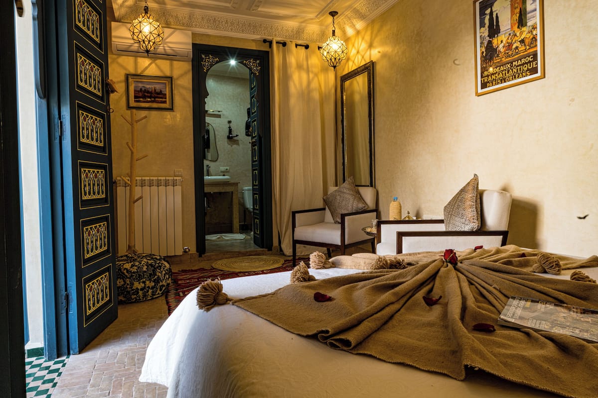 A hotel room with a bed, a chair, a table, and a mirror.