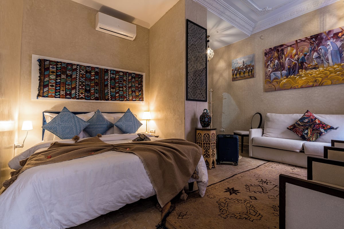 A hotel room with a bed, a sofa, a patterned rug, and artwork on the walls.
