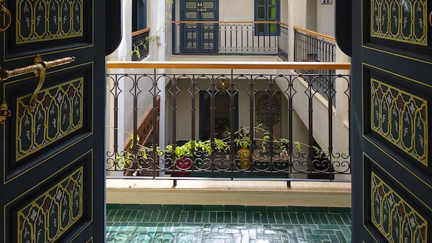 A courtyard with a tiled floor, a balcony with a railing, and a door with intricate designs. - Riad Atrium (Marrakech)