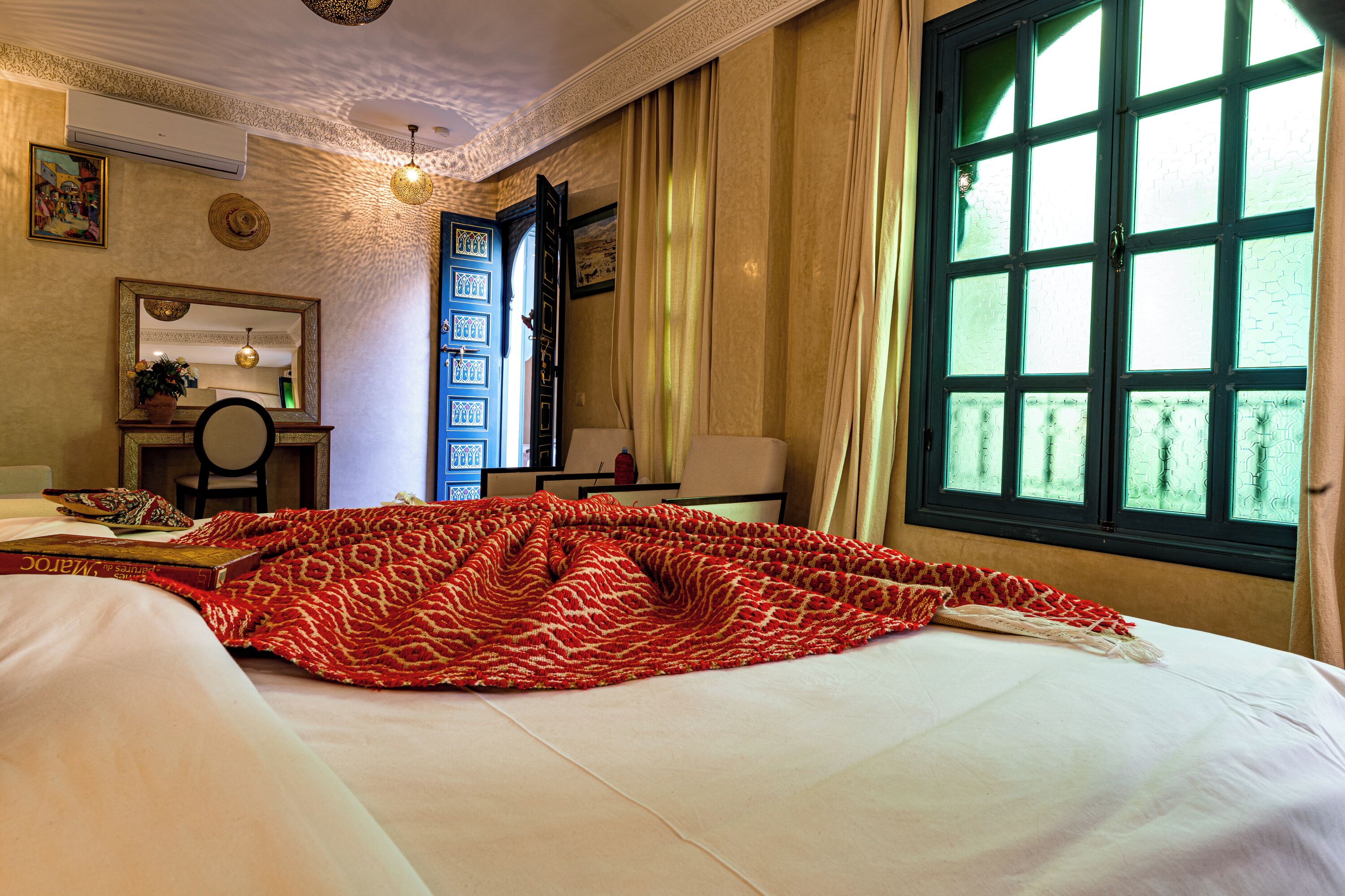 Habitación de hotel con cama, escritorio, silla, ventana con cortinas y pared con cuadros.