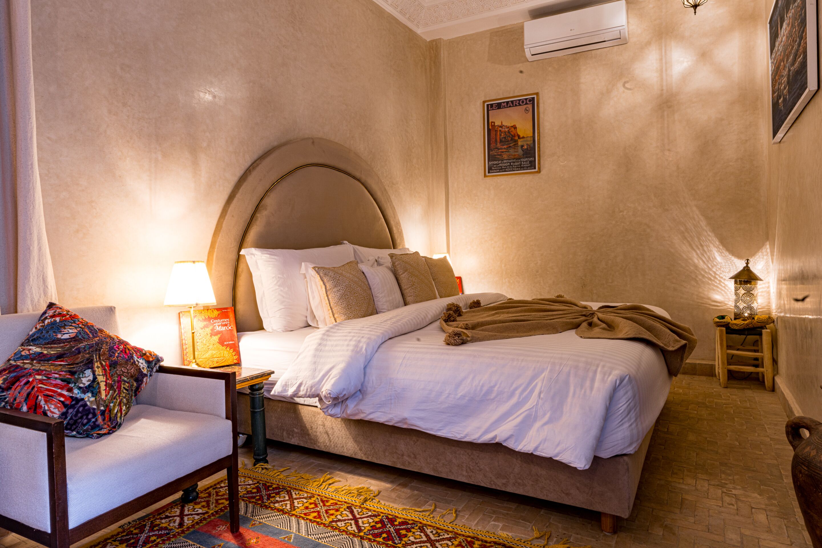 A hotel room with a bed, a chair, a lamp, and a poster on the wall.