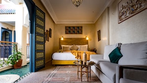 A bedroom with a bed, a sofa, a small table, a potted plant, and a patterned rug. - Riad Atrium (Marrakech)