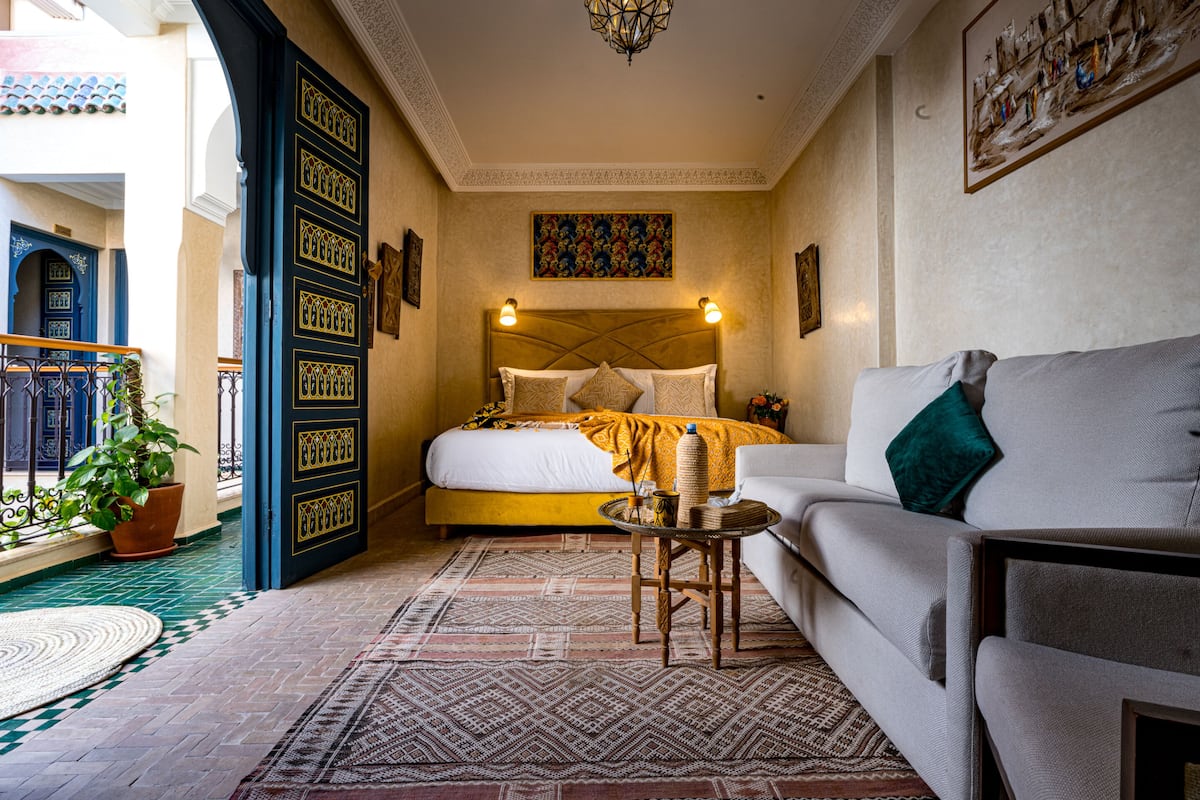 A bedroom with a bed, a sofa, a small table, a potted plant, and a patterned rug.
