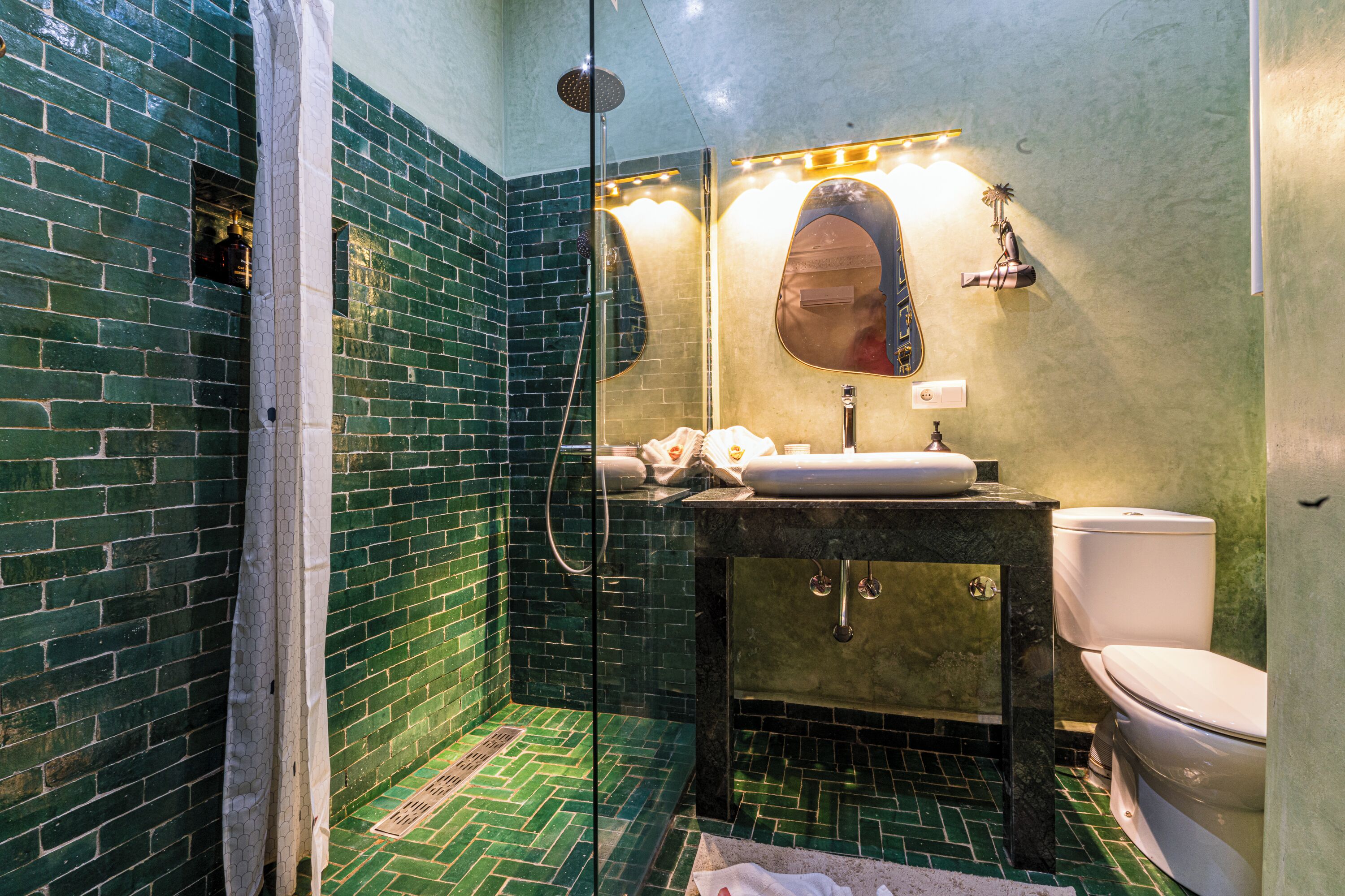 Un baño con ducha de azulejos verdes, un lavamanos con espejo y un inodoro.