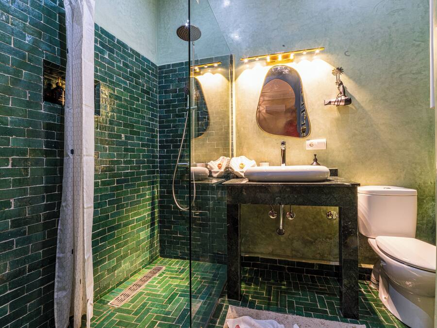Un baño con ducha de azulejos verdes, un lavamanos con espejo y un inodoro.