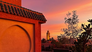 A courtyard with a tiled roof, potted plants, and a distant view of a tower against a sunset sky. - Riad Atrium (Marrakech)