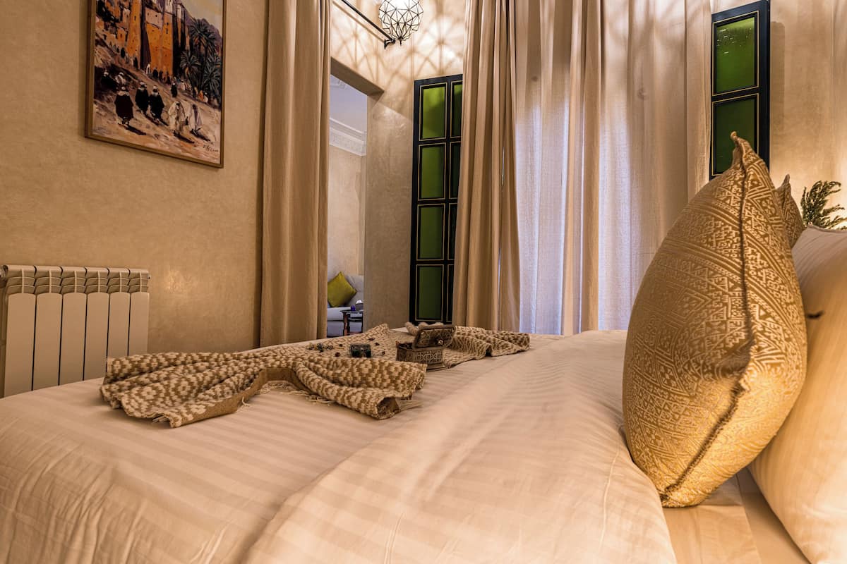 A neatly made bed with a patterned blanket, a large decorative pillow, and a painting on the wall.