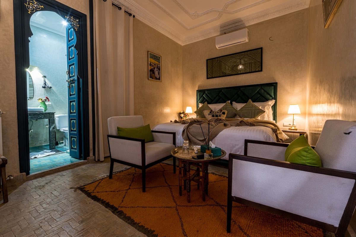 A hotel room with a bed, two armchairs, a small table, and a decorative mirror.