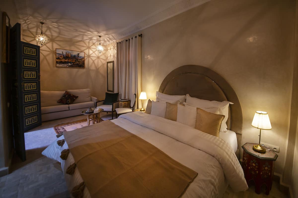 A hotel room with a large bed, a sofa, a small table, and a decorative lamp.