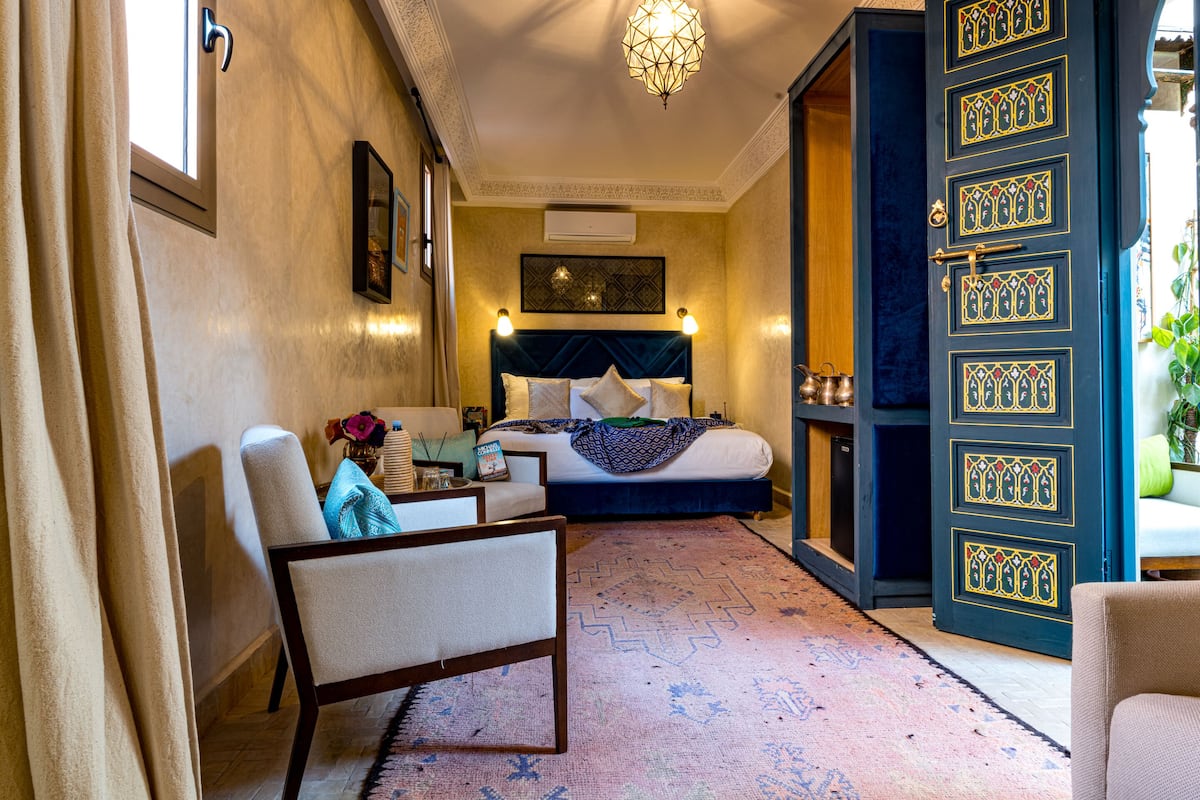 A hotel room with a bed, a chair, a table with a vase, and a decorative wall piece.