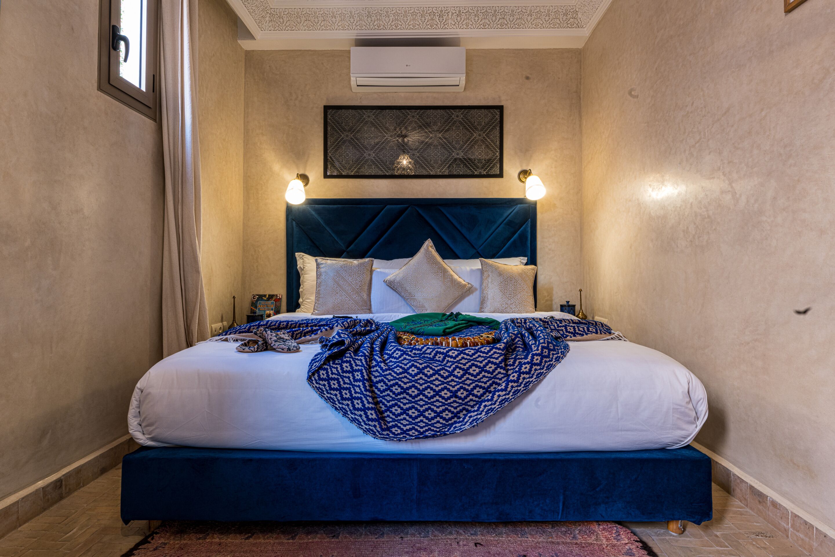 A neatly made bed with a blue headboard, white linens, and decorative pillows.