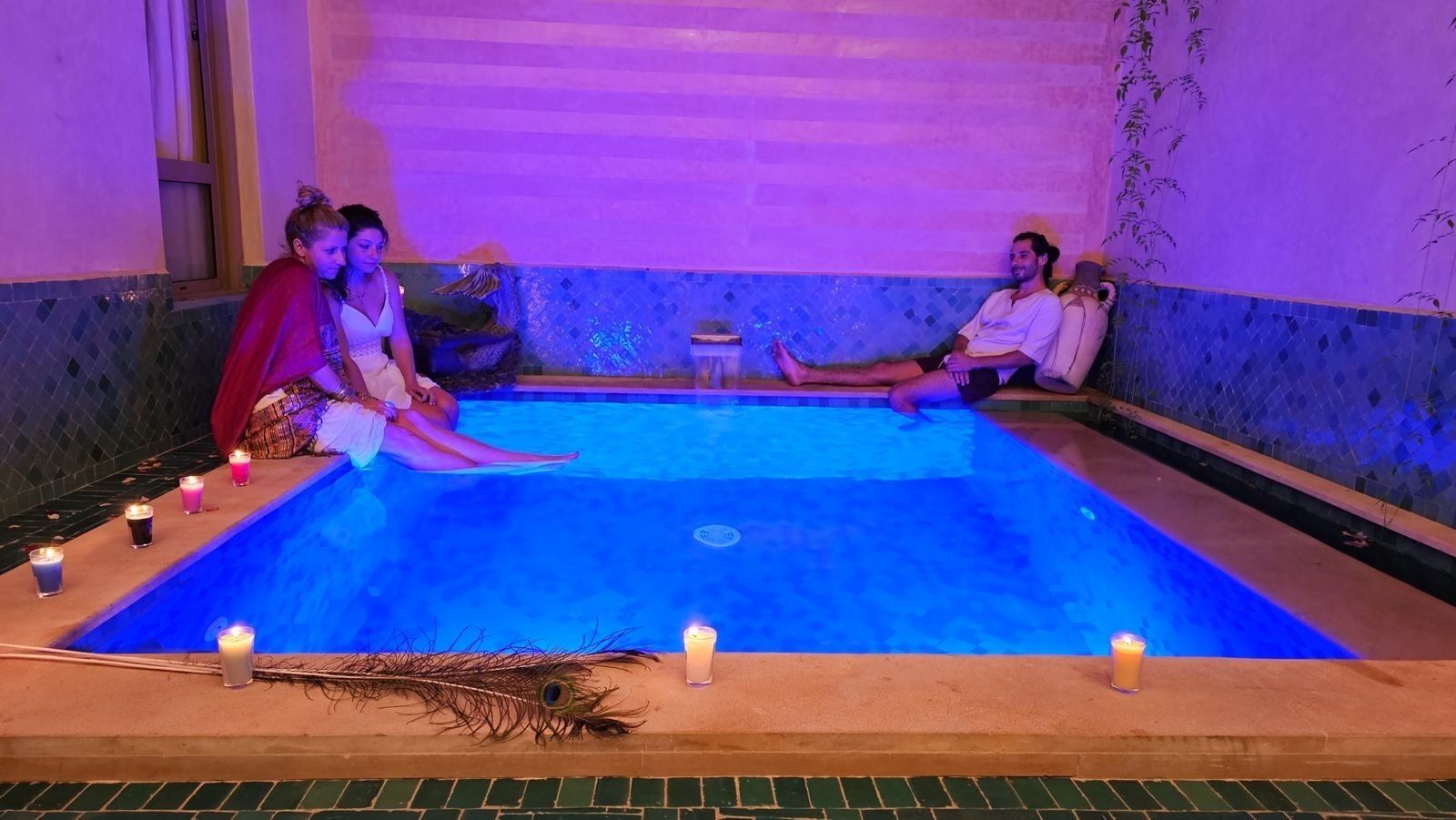 Un área de piscina con suelo de baldosas, una decoración con plumas de pavo real y velas.