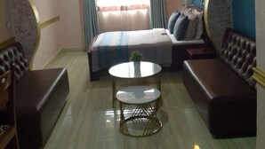 A bedroom with a bed, two sofas, a small table, and a TV. - CONSTELLATION HOTEL (Dschang)