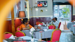 A restaurant with tables set for dining, chairs, and a television screen. - CONSTELLATION HOTEL (Dschang)