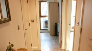 A hallway with wooden flooring, a mirror, a small table with a vase, and a trash bin. - Home In Birmingham New Street (Birmingham)