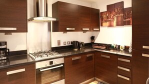 A modern kitchen with dark wood cabinets, stainless steel appliances, and a cityscape artwork on the wall. - Home In Birmingham New Street (Birmingham)
