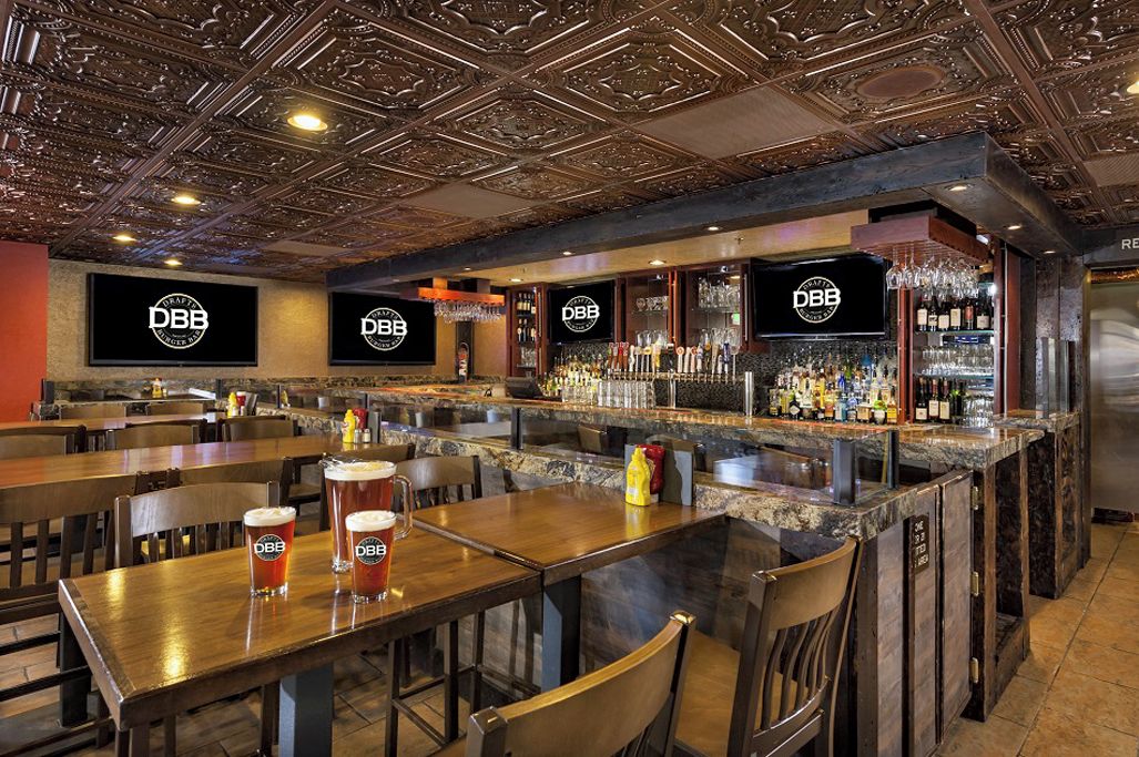 Zona de bar con varias mesas, mostradores y una variedad de botellas y vasos.