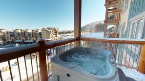 A hot tub on a balcony with a view of a residential area and mountains.