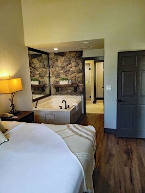 A hotel room with a large bed, a bathroom with a bathtub, and a stone wall.