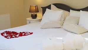 A neatly made bed with white linens, a heart-shaped arrangement of red rose petals, and two folded white towels. - Laguna House (Garkalnes novads)