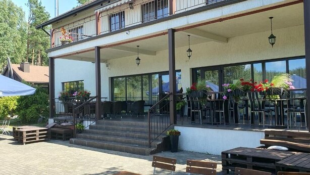 A two-story building with a covered outdoor seating area, wooden benches, and potted plants.