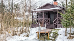 A wooden cabin with a metal staircase leading to a deck, surrounded by snow and trees. - Laguna House (Garkalnes novads)