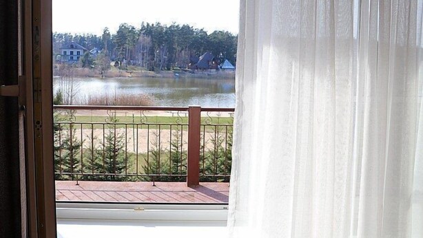 A view from a balcony with a metal railing, overlooking a body of water and a forested area. - Laguna House (Garkalnes novads)