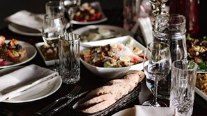 A dining table set with various dishes, glasses, and a basket of bread.