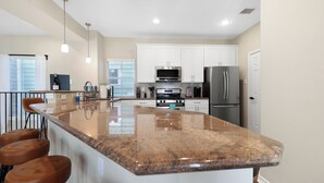 A modern kitchen with white cabinets, stainless steel appliances, a granite countertop, and bar stools. - Tranquil Heights / Stylish Boho Retreat / King Bed / Long term stay (Houston)