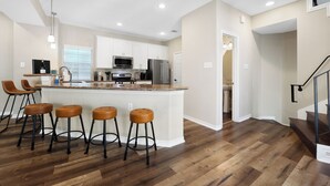 A modern kitchen with a central island, bar stools, and a staircase leading to an upper level. - Tranquil Heights / Stylish Boho Retreat / King Bed / Long term stay (Houston)
