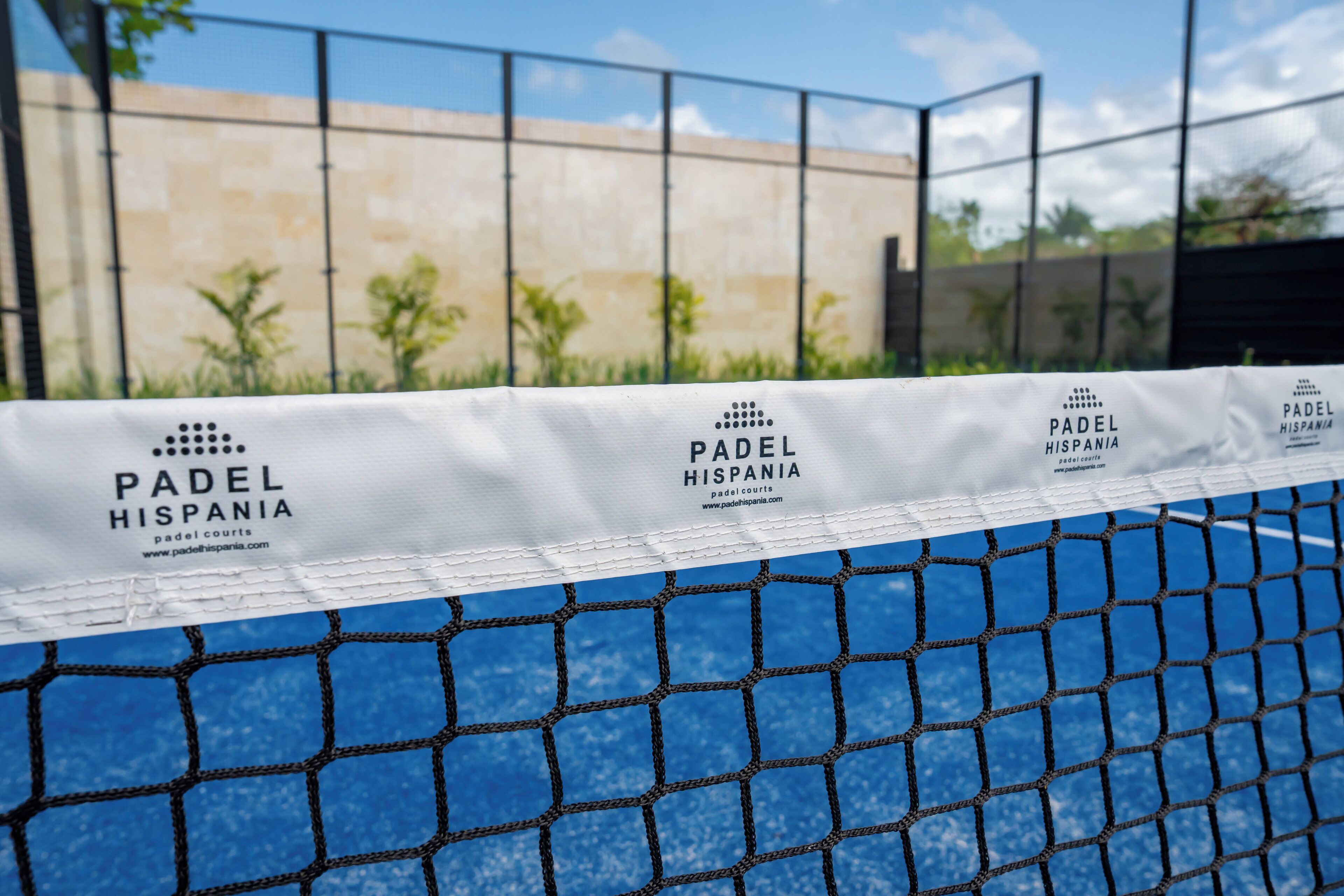 Una cancha de tenis con una red y un cartel con la marca 'PADEL HISPANIA'.