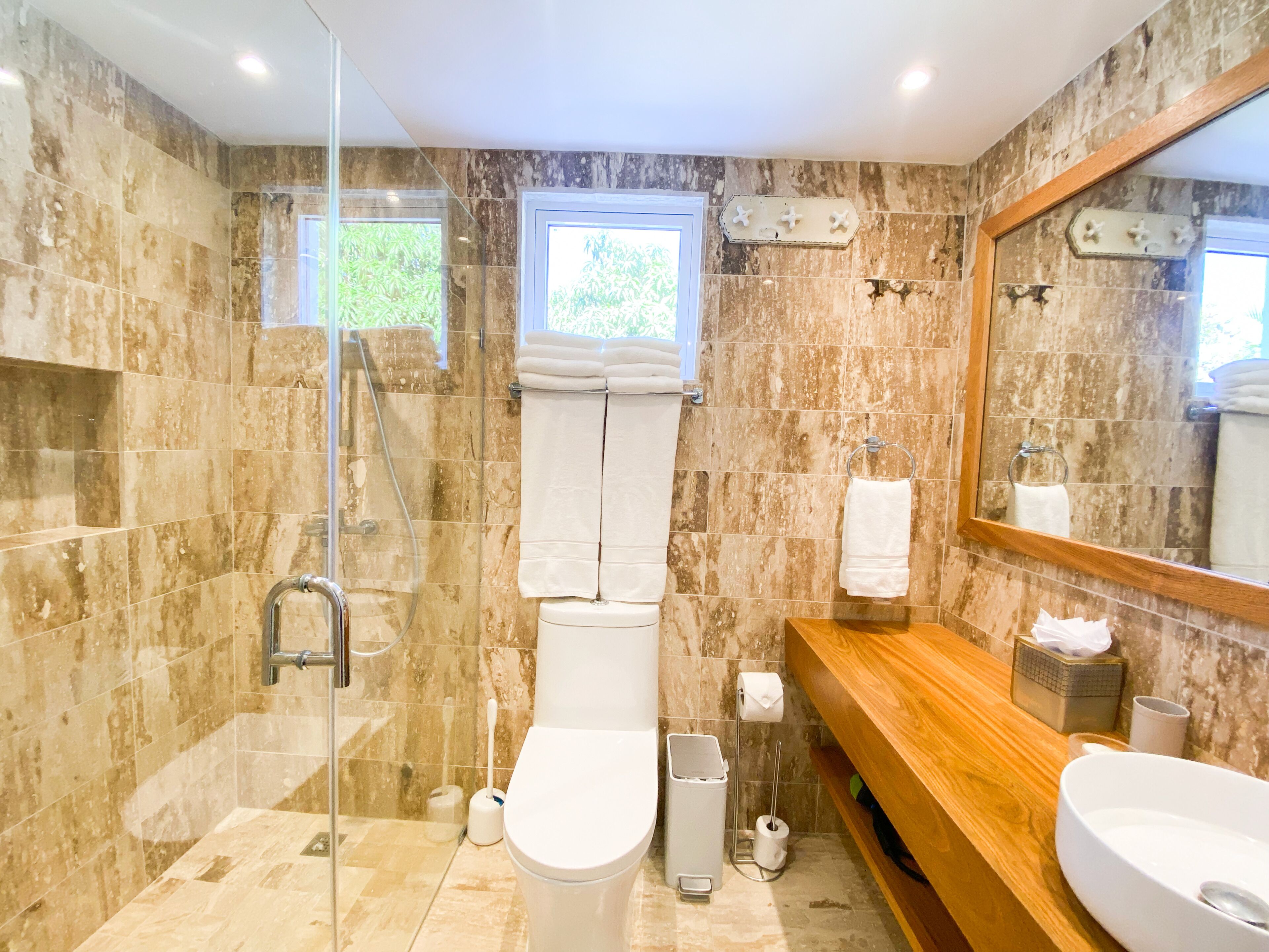 Un baño moderno con ducha envuelta en vidrio, tocador de madera, dos lavamanos y un espejo grande.