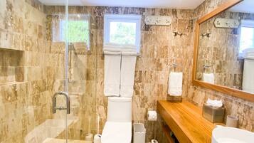 Un baño moderno con ducha envuelta en vidrio, tocador de madera, dos lavamanos y un espejo grande.