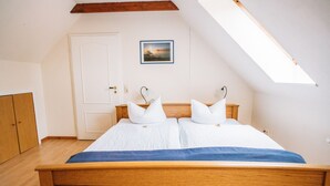 Une chambre à coucher avec un lit en bois, du linge de lit blanc, une lucarne, une porte et un tableau encadré au mur.