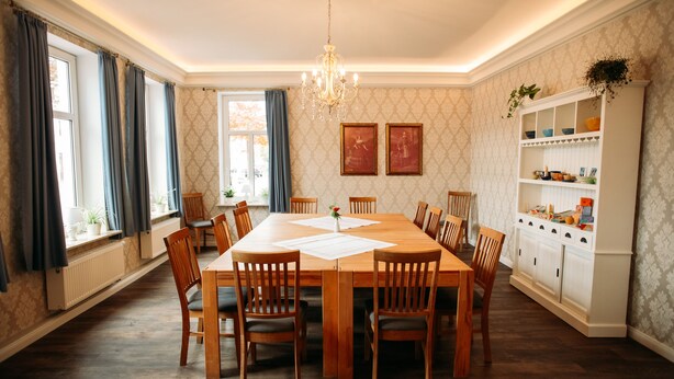 Une salle à manger avec une grande table en bois, des chaises, un lustre et un buffet avec des étagères.