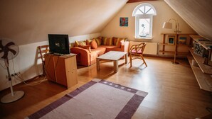Une pièce mansardée chaleureuse, avec un plafond en pente, un plancher en bois, un canapé, une table basse, un ventilateur et une fenêtre offrant une belle vue.