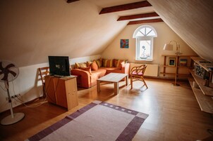 Um quarto de sótão acolhedor com teto inclinado, chão de madeira, sofá, mesa de centro, ventoinha e janela com vista.