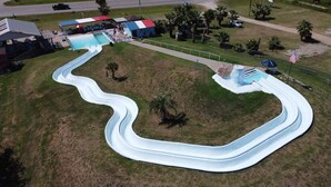 Vista aérea de un parque acuático con un tobogán serpenteante, una piscina y zonas verdes circundantes con palmeras.