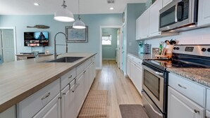 Een moderne keuken met witte kastjes, een groot eiland, roestvrijstalen apparatuur en een flatscreen televisie.