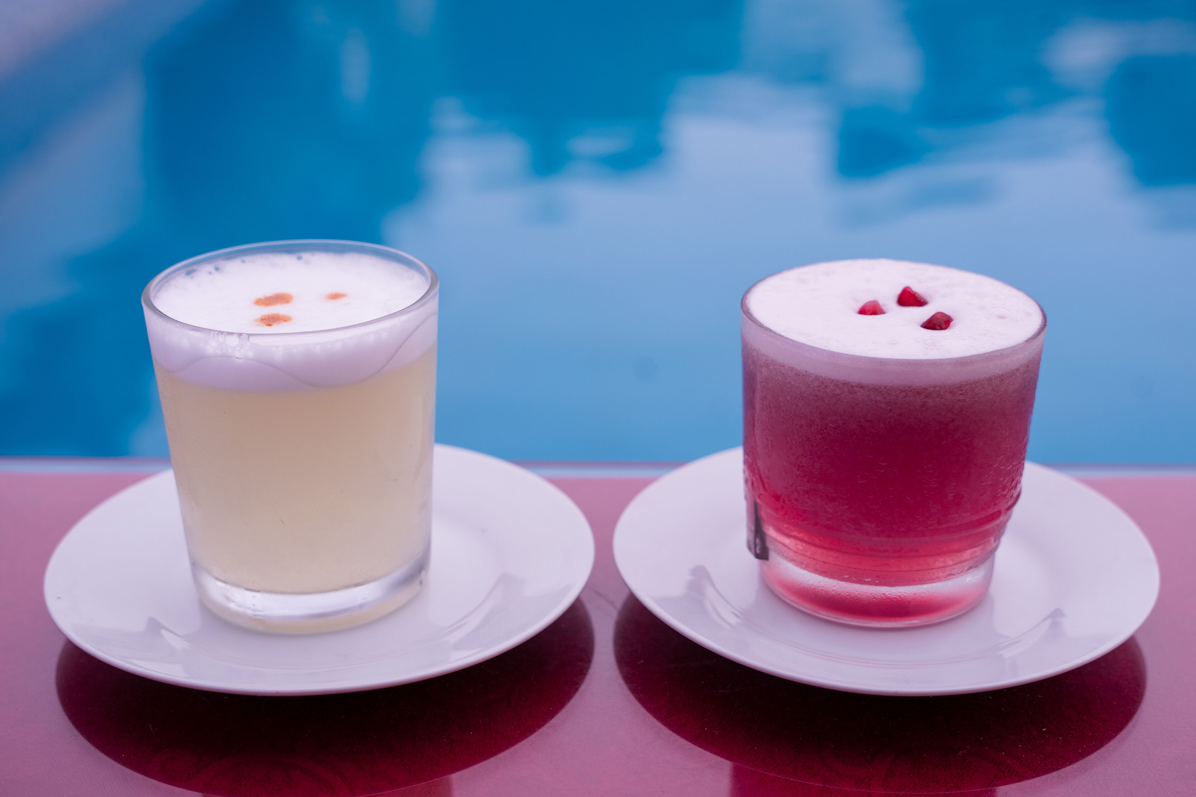 Dos vasos de bebidas sobre platillos blancos junto a una piscina.