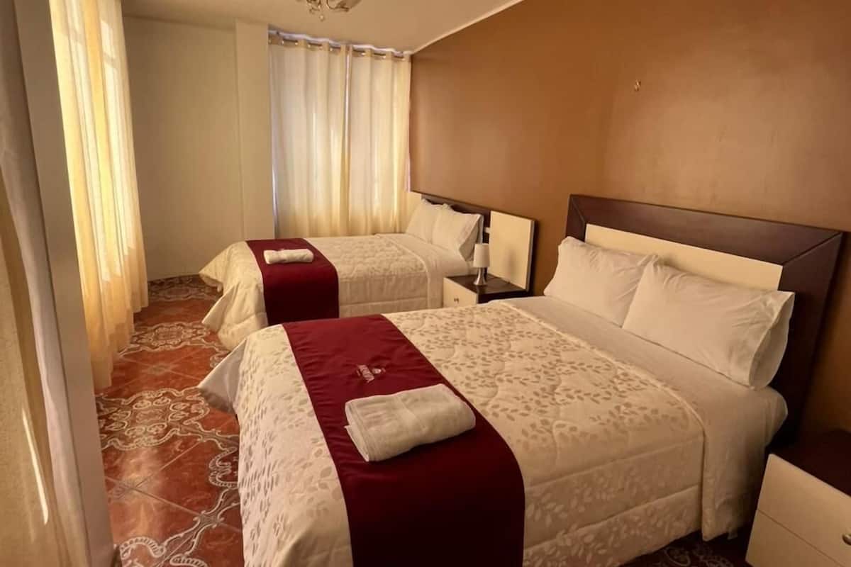 A hotel room with two beds, a nightstand, a lamp, and a patterned floor.